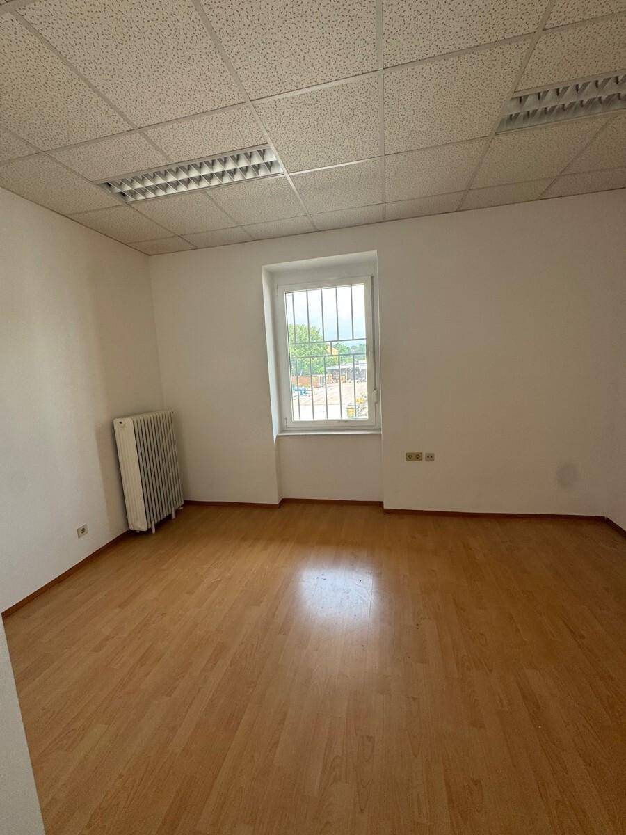 Helles Einzelbüro mit Holzfußboden, einem Fenster mit Gitter und einem Heizkörper.