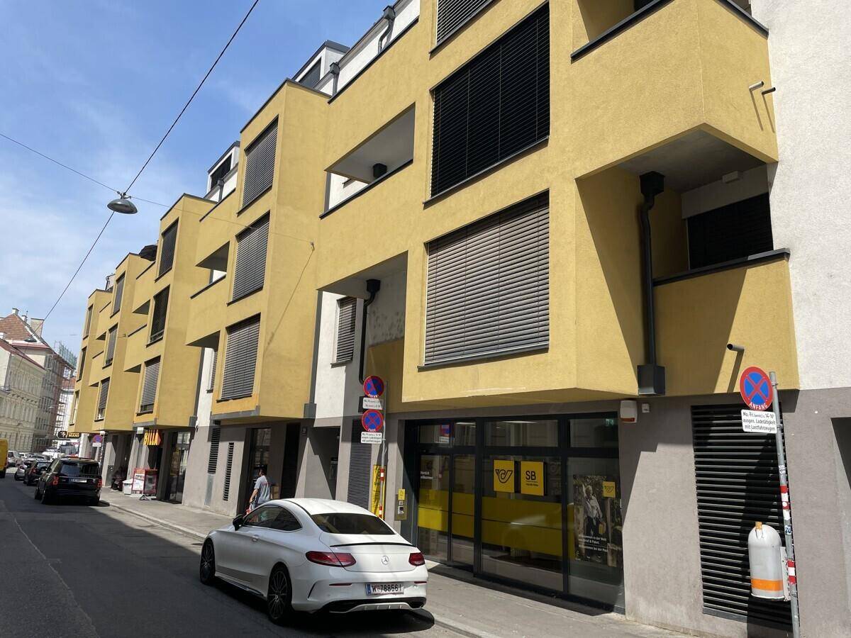 Modernes Gebäude mit gelber Fassade, großen Fenstern und Geschäften im Erdgeschoss.