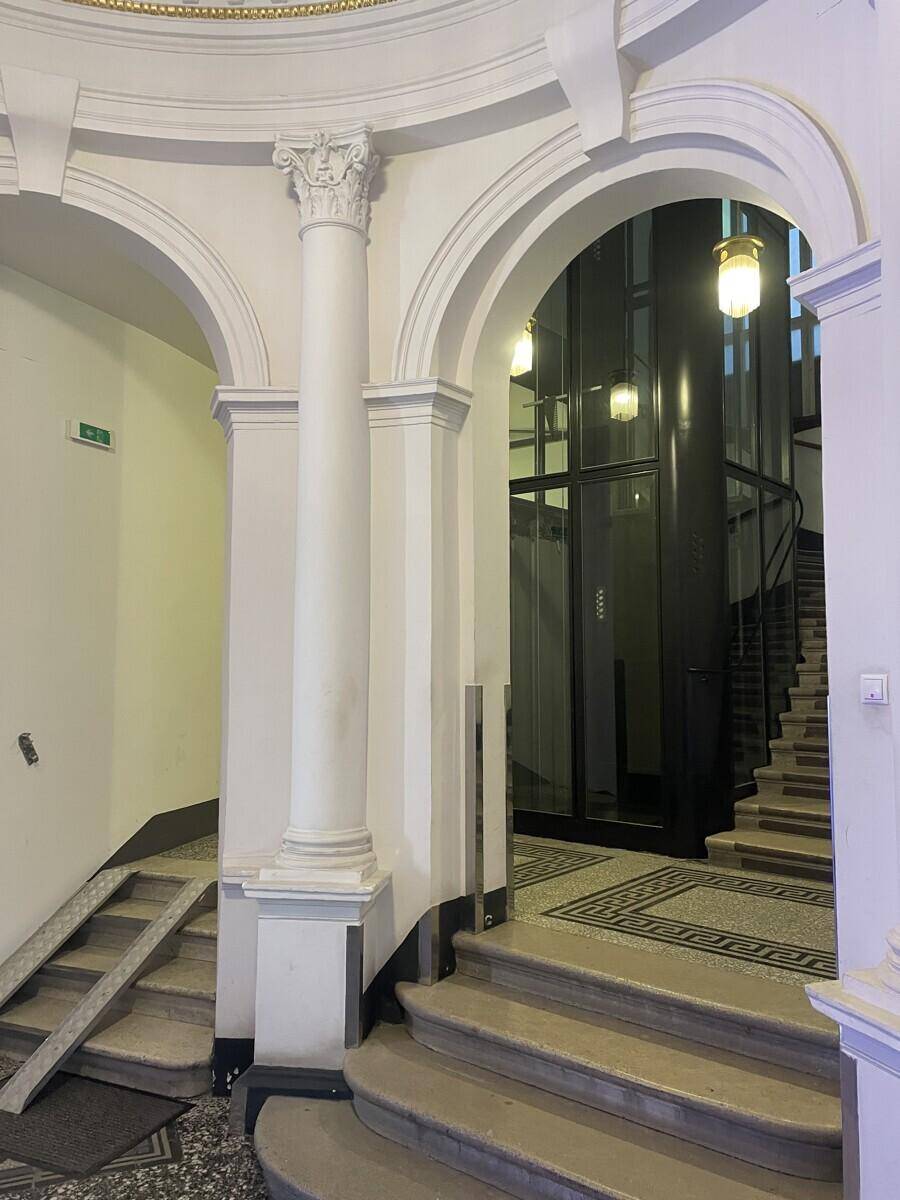 Detailansicht des eleganten Eingangsbereichs mit Säulen, Bögen und einem modernen Glasaufzug.