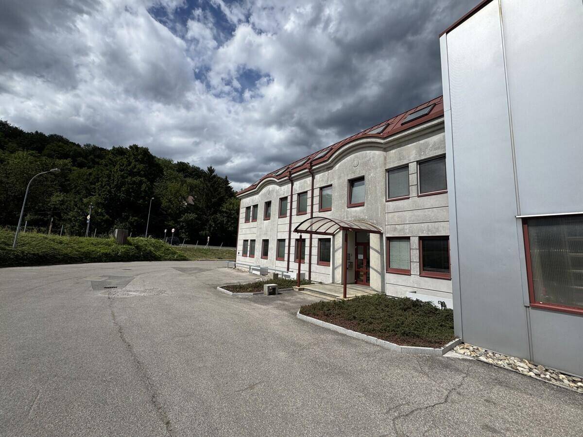 Außenansicht des Bürogebäudes mit großem Parkplatz und bewaldetem Hügel im Hintergrund.