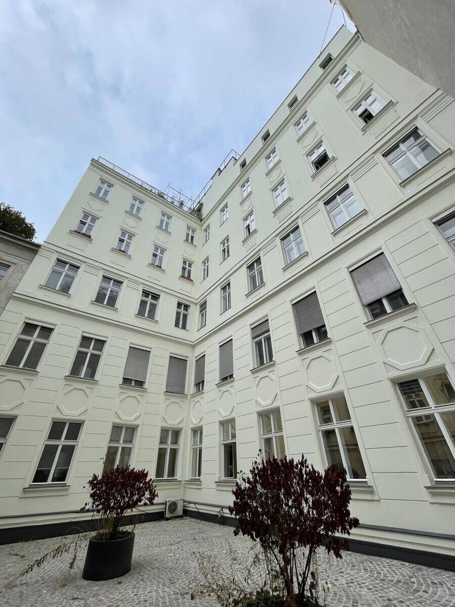 Innenhof eines Wohngebäudes mit Kopfsteinpflaster und kleinen Pflanzen unter bewölktem Himmel.