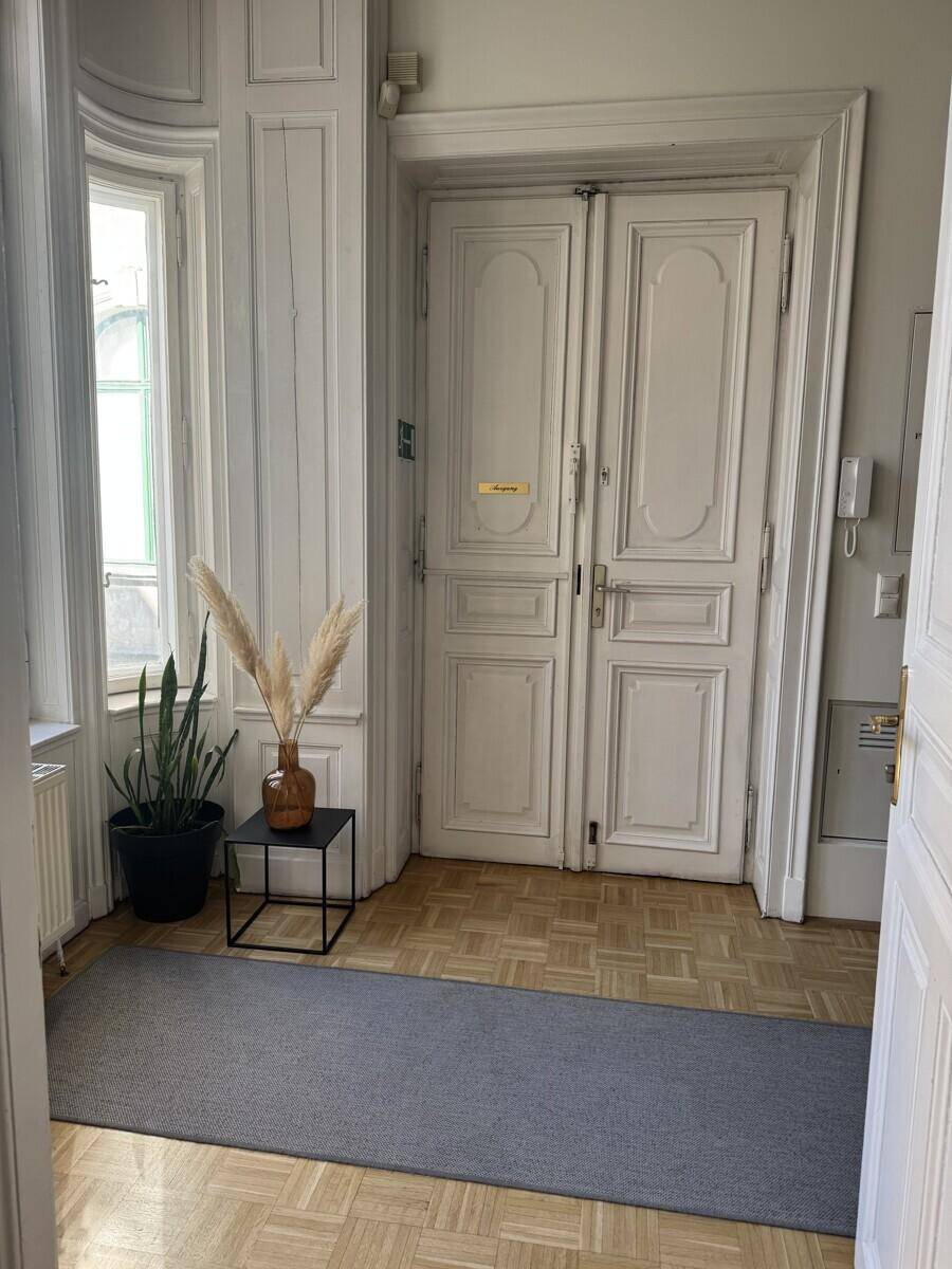 Heller Eingangsbereich mit Fischgrätparkett, hohen weißen Doppeltüren und einem Fenster, das natürliches Licht hereinlässt.