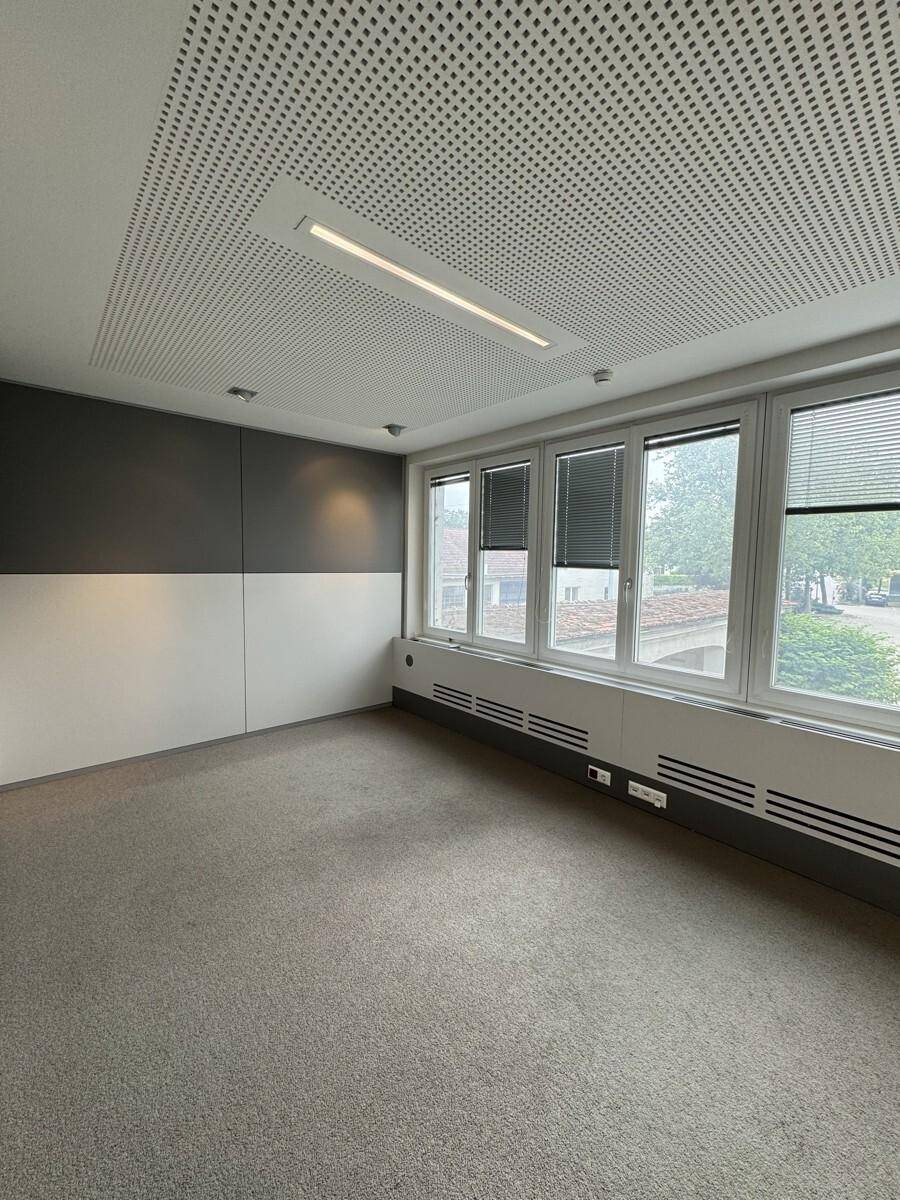 Modernes Büro mit perforierter Decke, Teppichboden und großen Fenstern mit Jalousien, bietet eine angenehme Arbeitsumgebung.