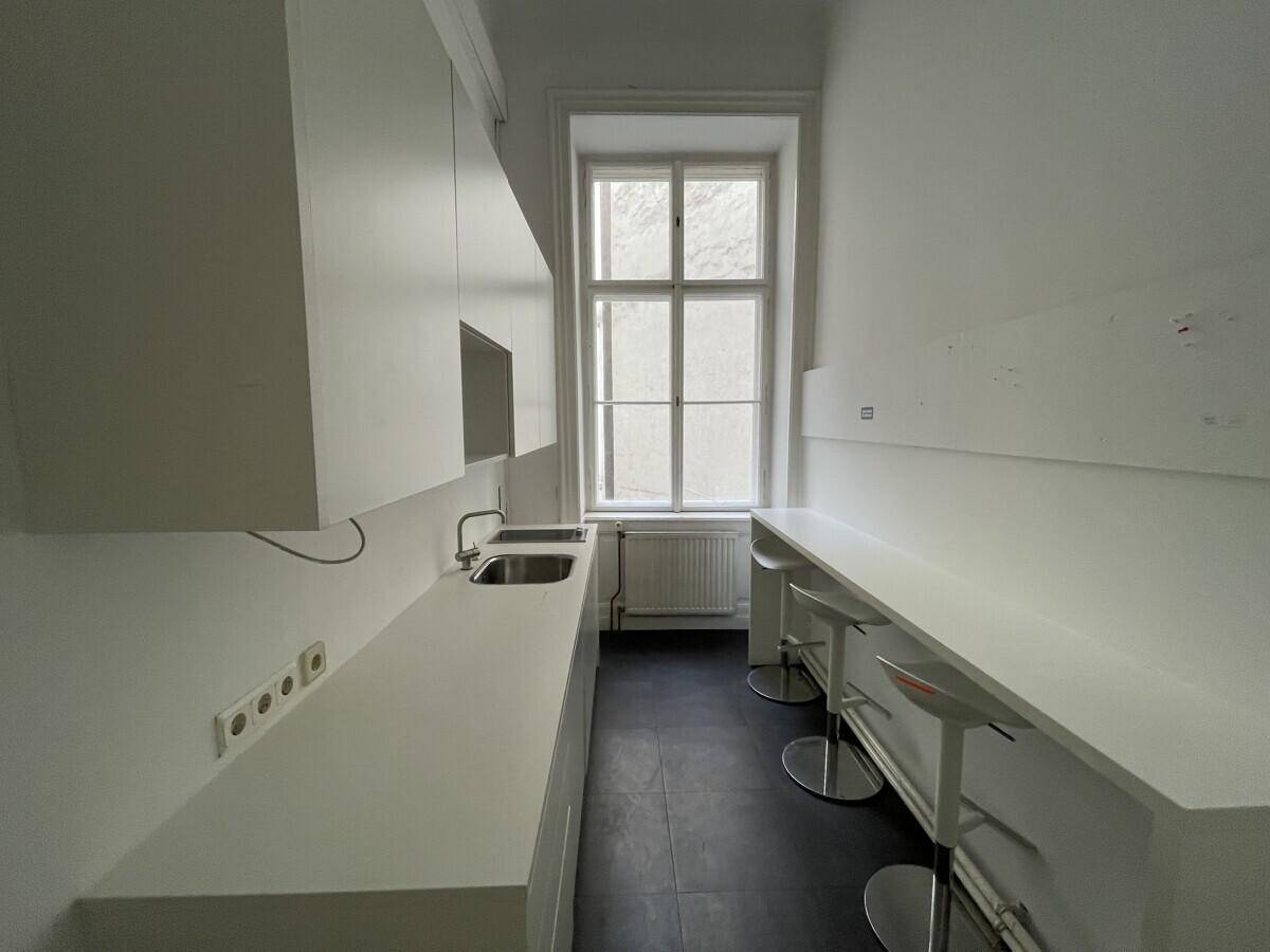 Schmale Küchenzeile mit weißer Arbeitsplatte, Spüle und einer langen Theke mit Barhockern.