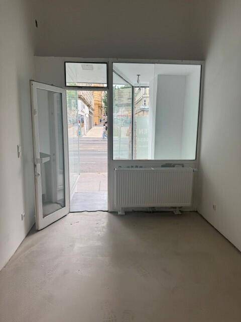 Innenansicht eines Ladenlokals mit großen Schaufenstern zur Straße und einem Heizkörper unter dem Fenster.