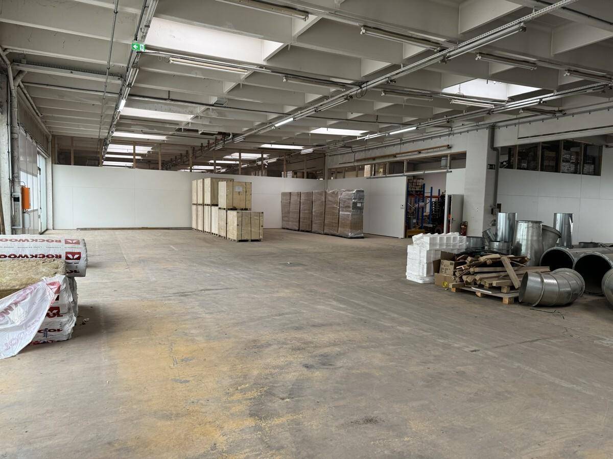 Geräumige Industriehalle mit Betonboden, hohen Decken und gestapelten Materialien im Hintergrund.