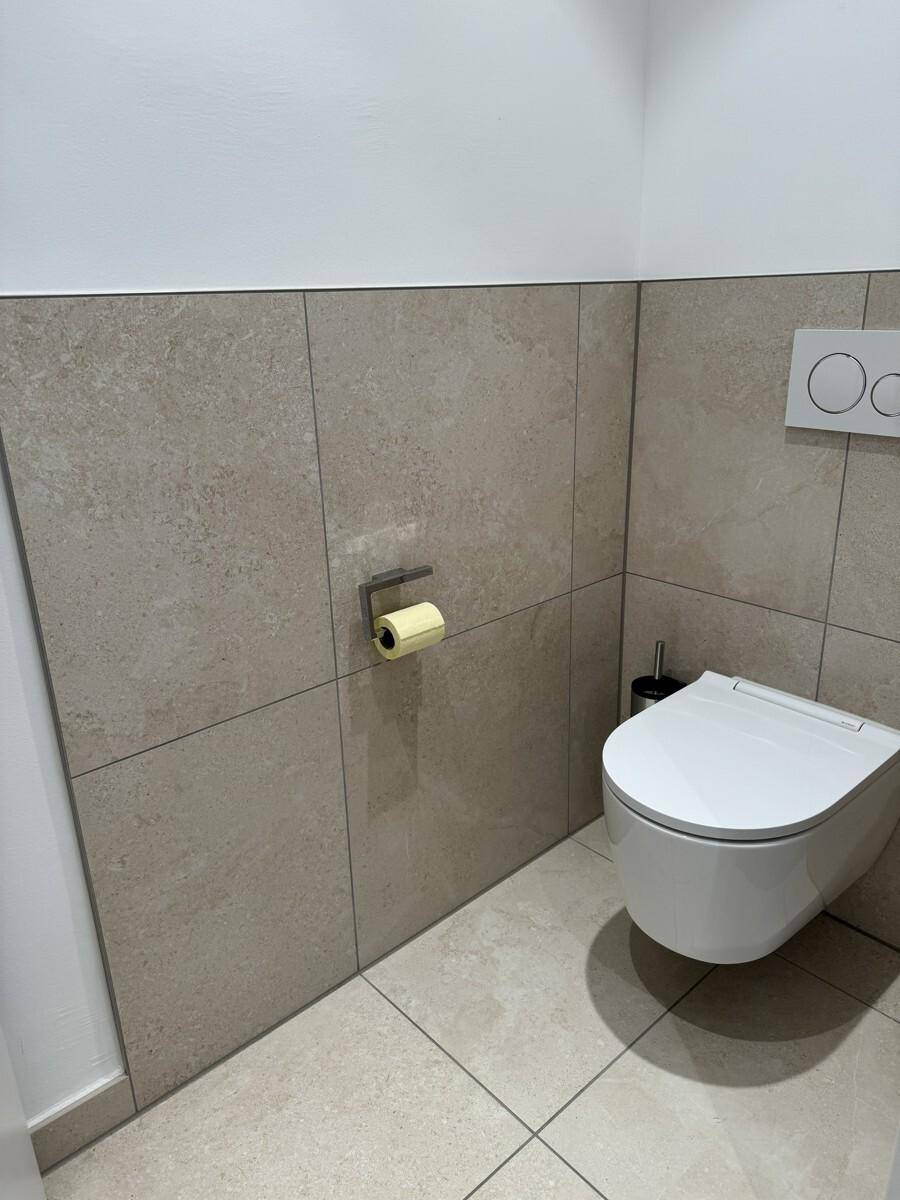 Modernes WC mit wandhängender Toilette und beigefarbenen Fliesen an Wänden und Boden, sehr gepflegt.