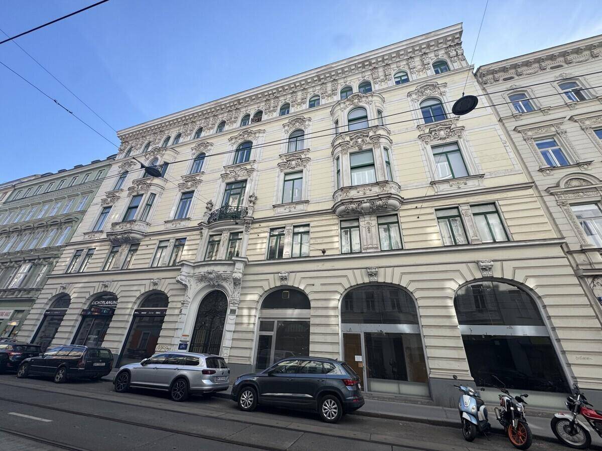 Historisches Gebäude mit reich verzierter Stuckfassade und großen Fenstern an einer belebten Stadtstraße.