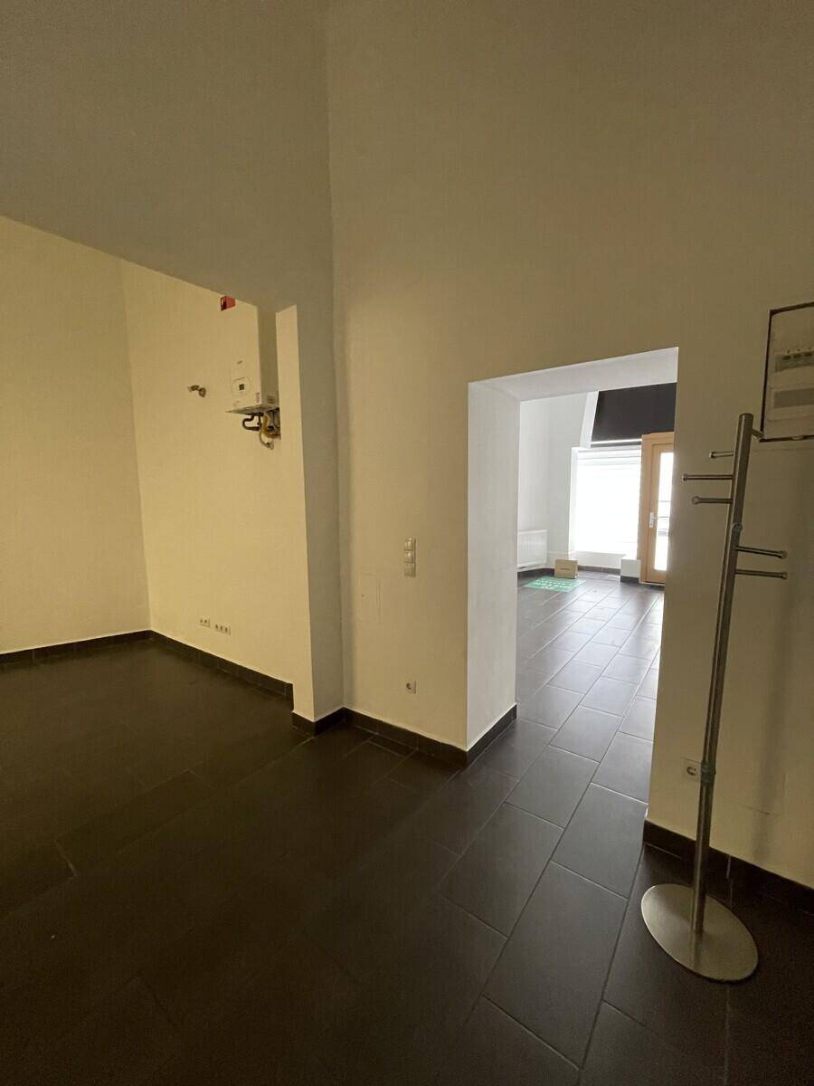 Blick durch den Gewerberaum vom hinteren Bereich zum Eingang, mit dunklem Fliesenboden und weißen Wänden.