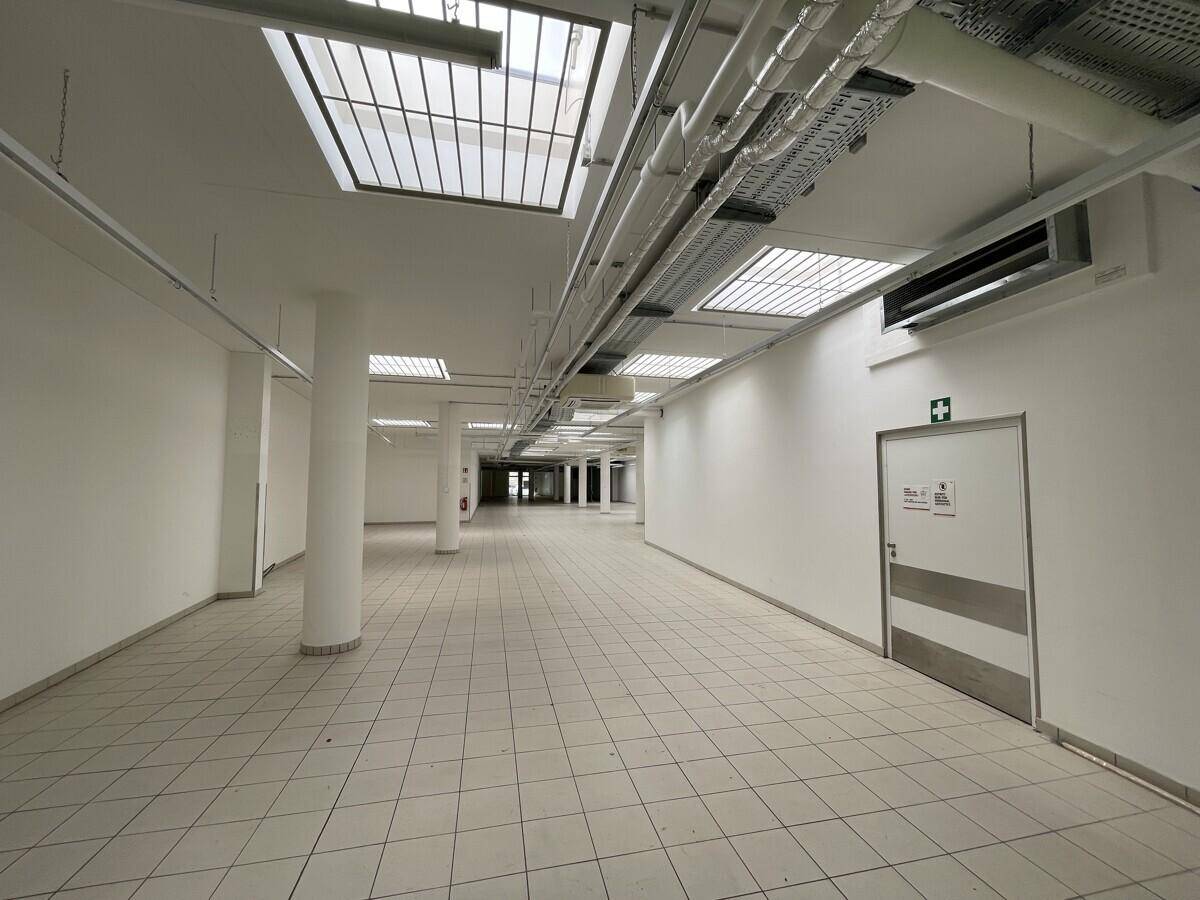 Langer, heller Gewerberaum mit Fliesenboden, Deckenfenstern und einer Notausgangstür.