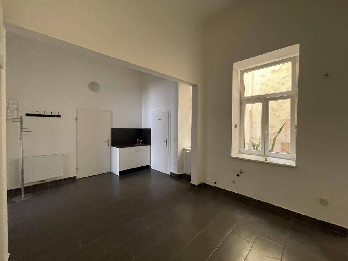 Innenansicht eines Gewerberaums mit kleiner Küchenzeile und einem Fenster, das Licht hereinlässt.