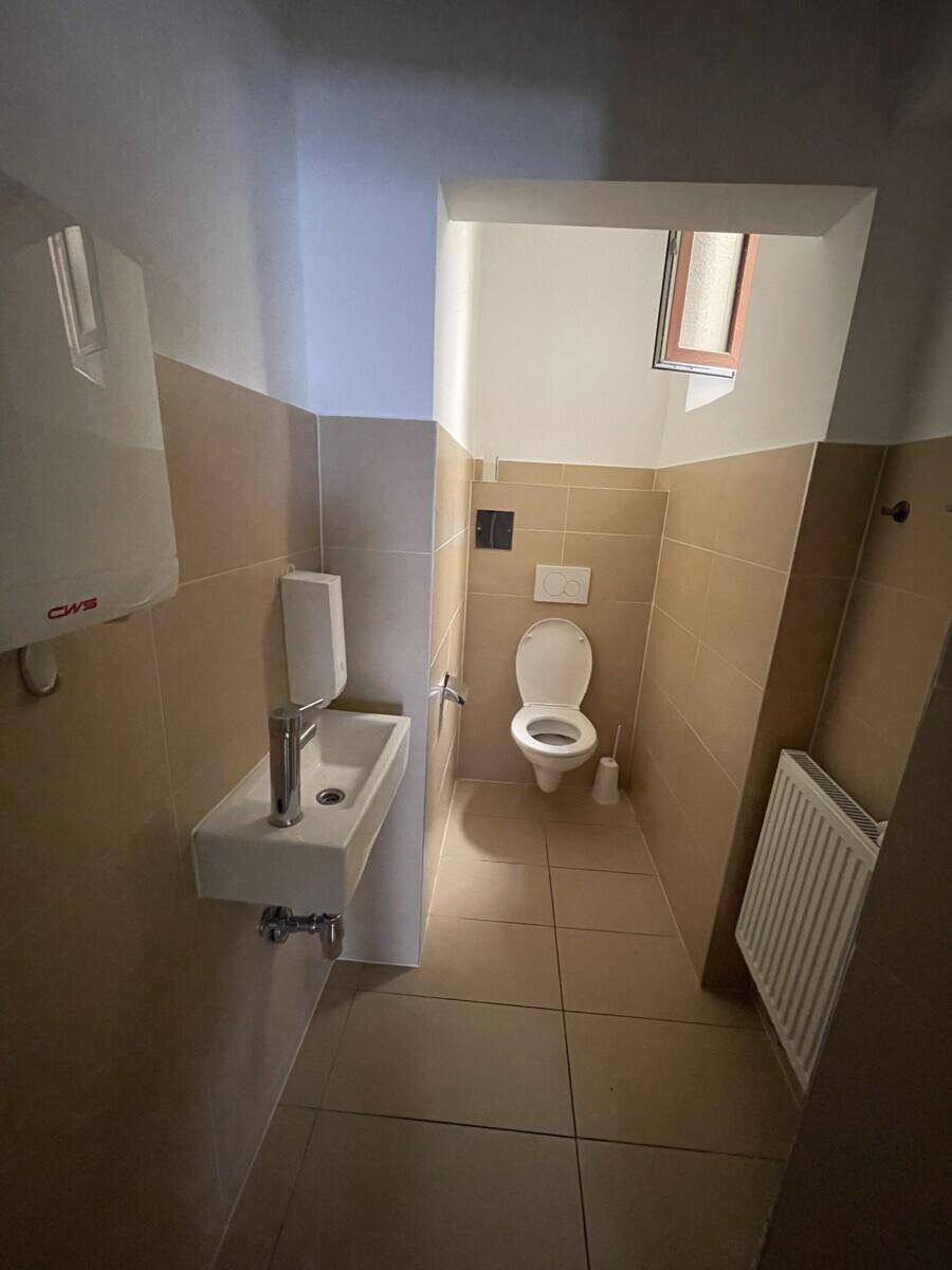 Kleiner Toilettenraum mit beigefarbenen Fliesen, einem WC, Waschbecken und einem kleinen Fenster.
