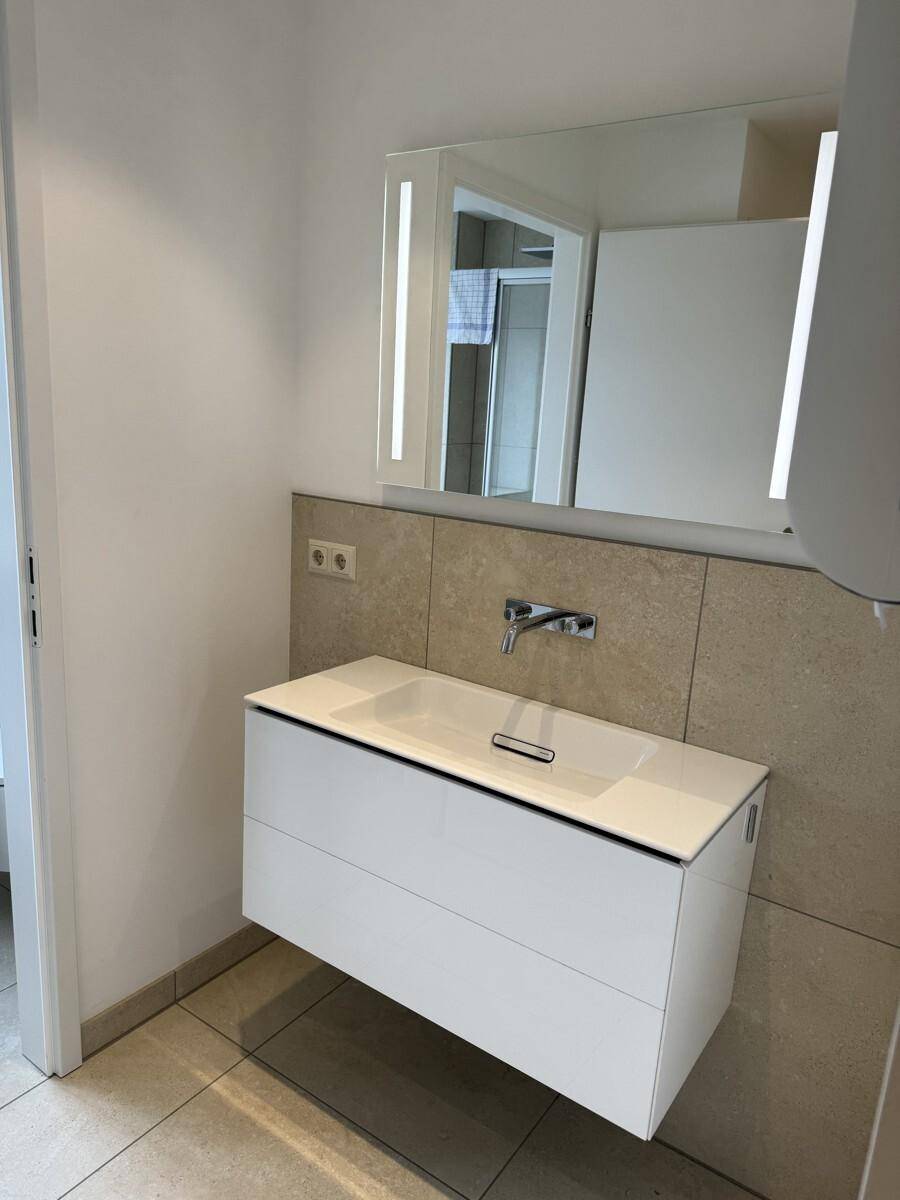 Modernes Badezimmer mit schwebendem Waschtisch, beleuchtetem Spiegel und beigefarbenen Fliesen, sehr gepflegt.