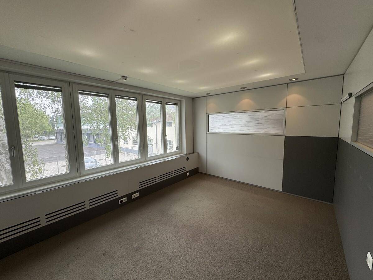 Helles Büro mit großen Fenstern und Teppichboden, ausgestattet mit modernen Wandpaneelen und integrierter Beleuchtung.
