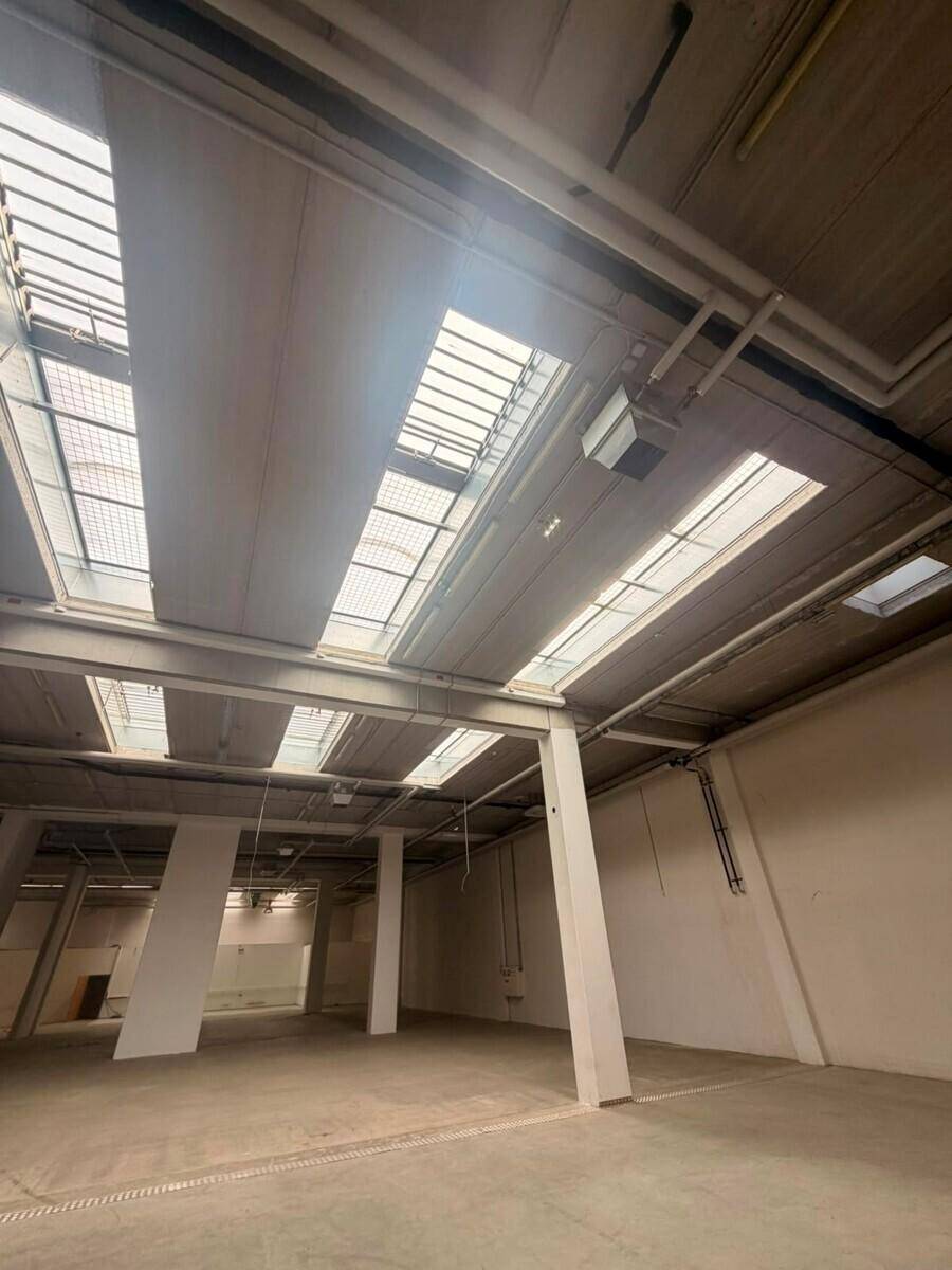 Geräumiger Industrieraum mit Betonboden, hohen Decken und zahlreichen Oberlichtern für Tageslicht.
