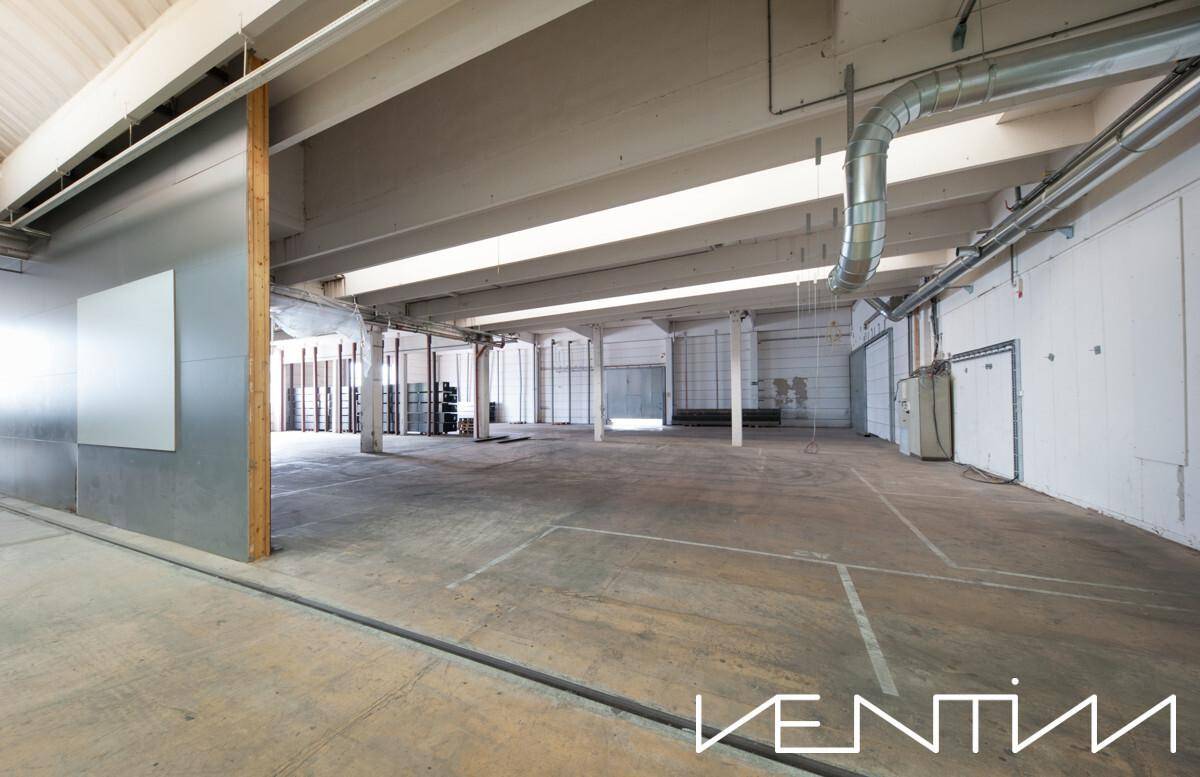 Weitläufige, leere Lagerhalle mit Betonboden und sichtbaren Lüftungsrohren an der Decke, bereit zur Nutzung.