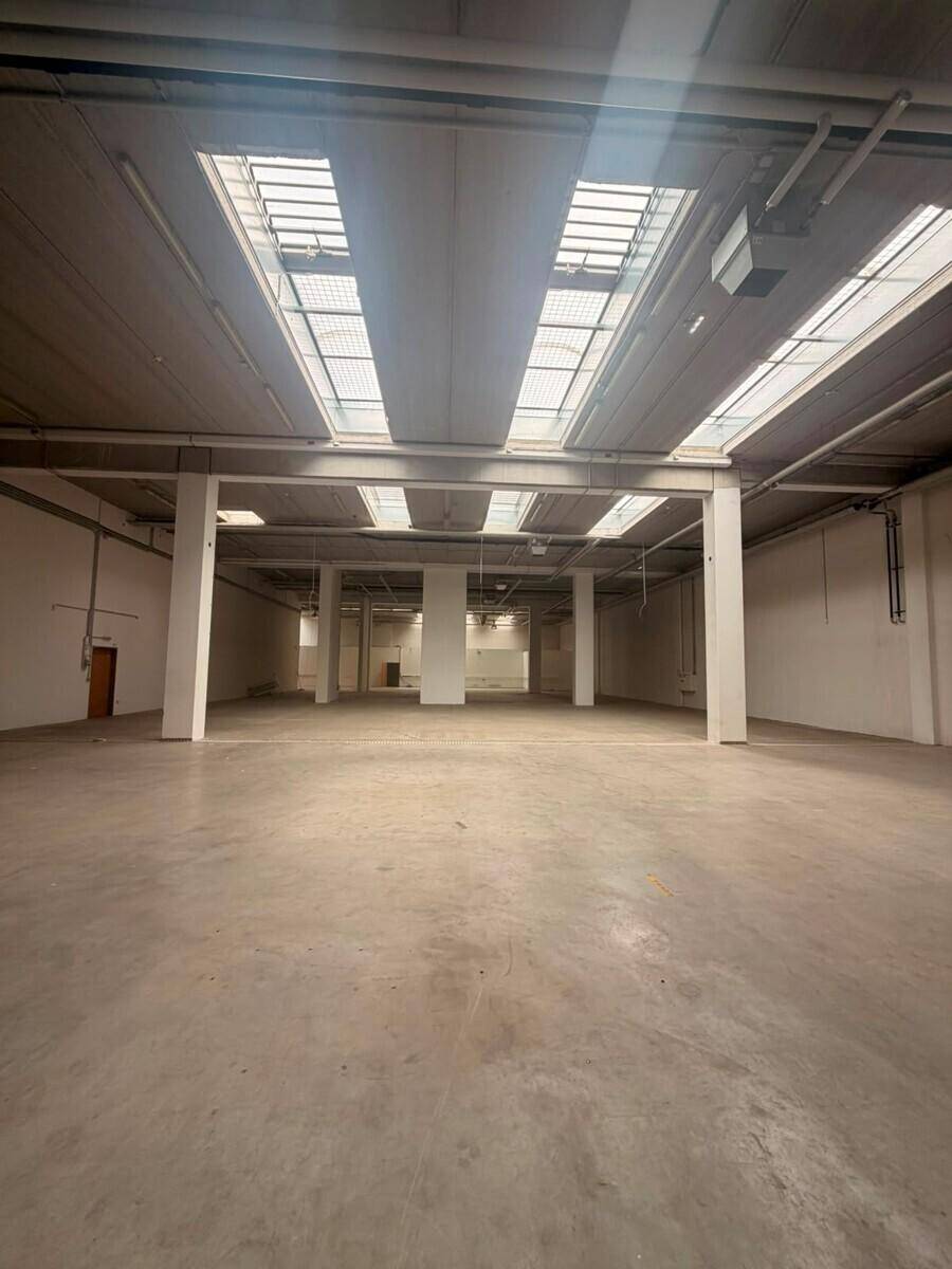 Weitläufiger, leerer Industrieraum mit Betonboden, hohen Decken und vielen Oberlichtern für Helligkeit.