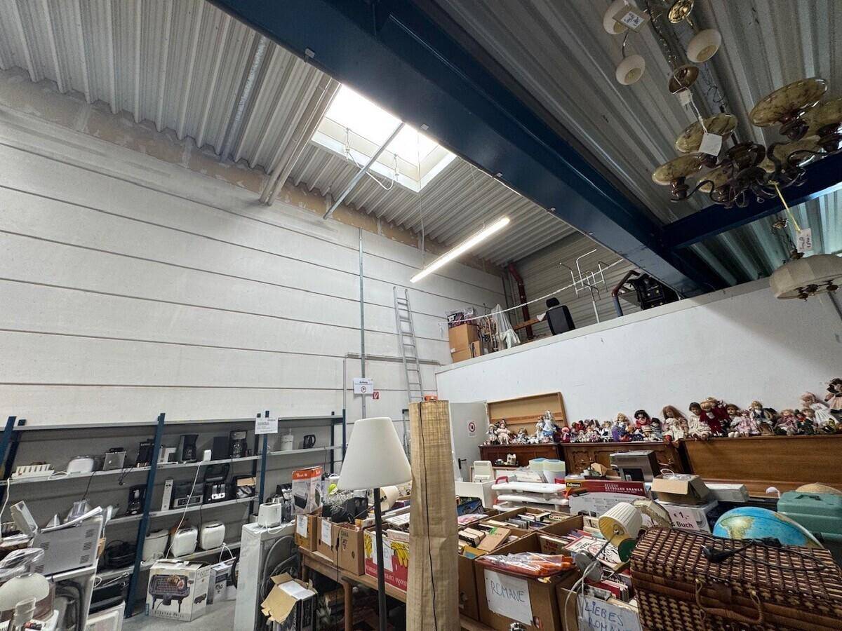 Innenansicht eines Verkaufsraums mit hoher Decke, Oberlicht und einer Vielzahl von Artikeln auf Regalen und Tischen.