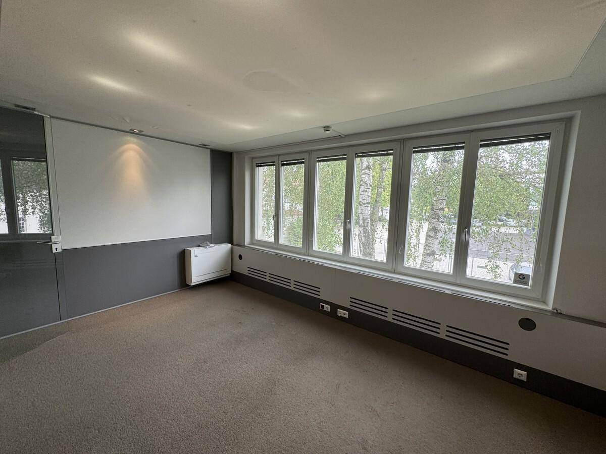 Leeres Büro mit Teppichboden und großen Fenstern, die eine grüne Aussicht bieten, ideal für eine flexible Gestaltung.