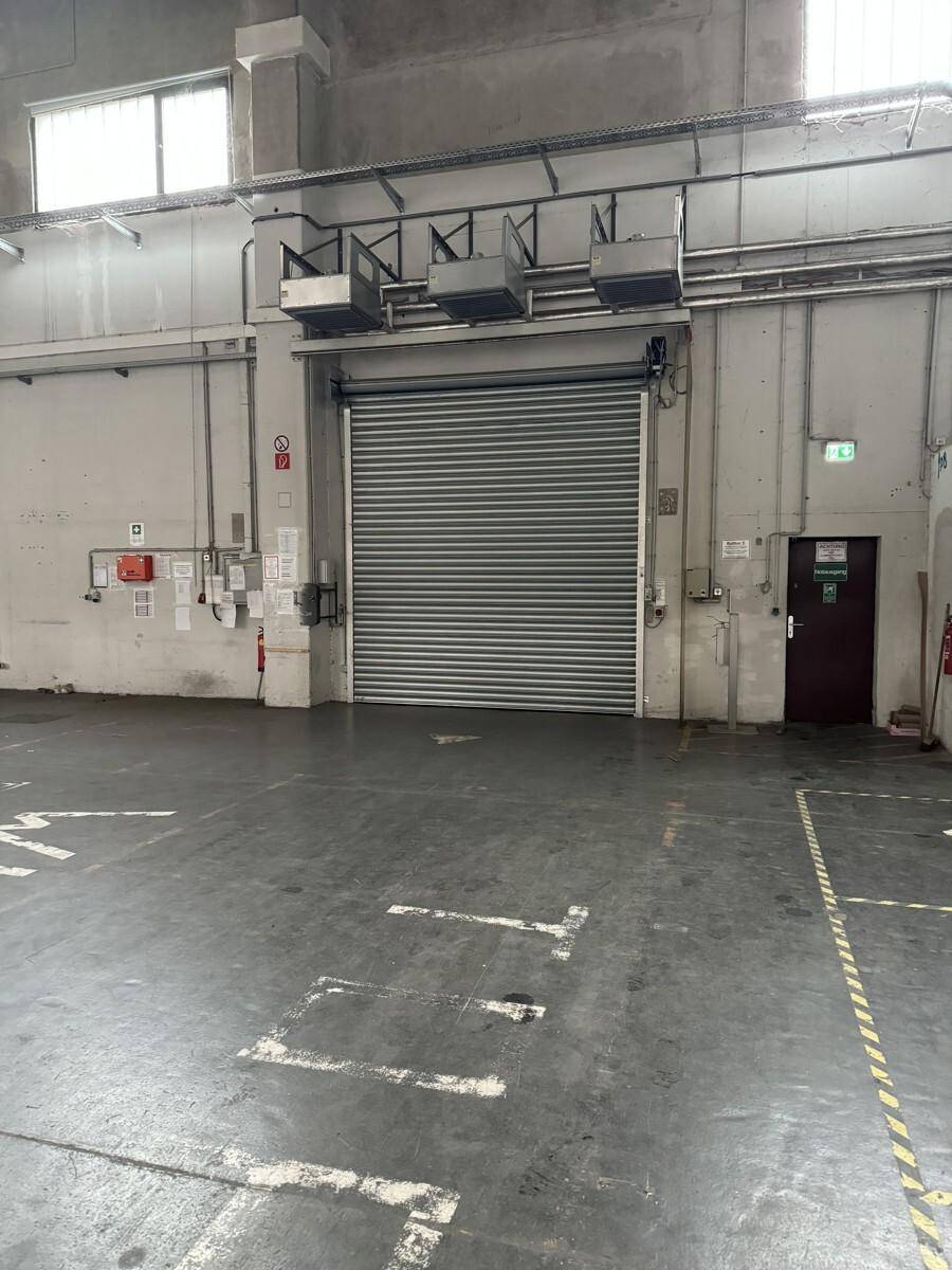 Industrierolltor in einer Lagerhalle mit Betonboden und Sicherheitskennzeichnungen an der Wand.