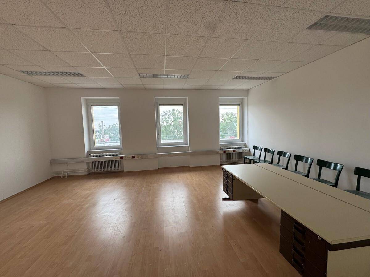 Geräumiges Büro mit Holzfußboden, drei Fenstern und einem langen Schreibtisch mit Stühlen.