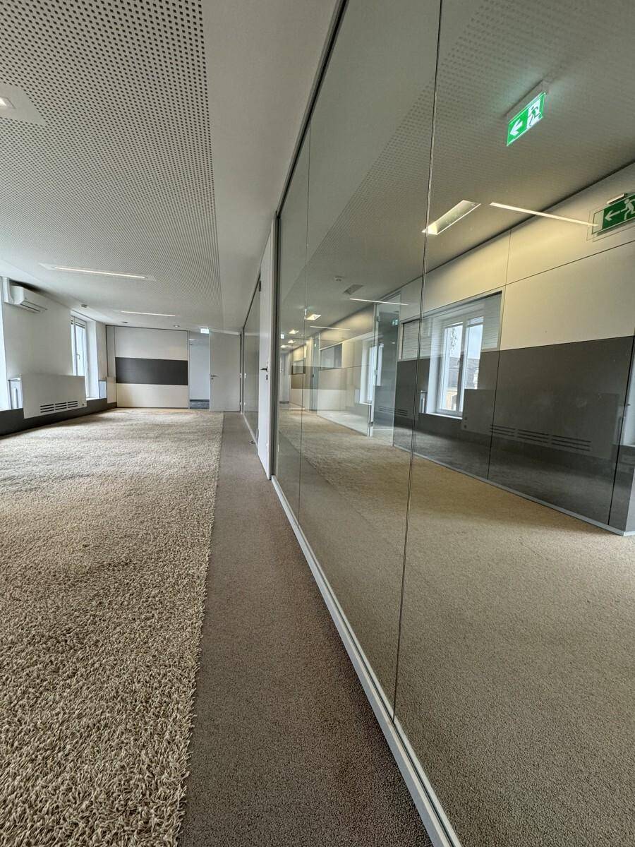 Langer Bürogang mit Teppichboden und Glaswänden, die zu weiteren Büroräumen führen, sorgt für eine offene Atmosphäre.