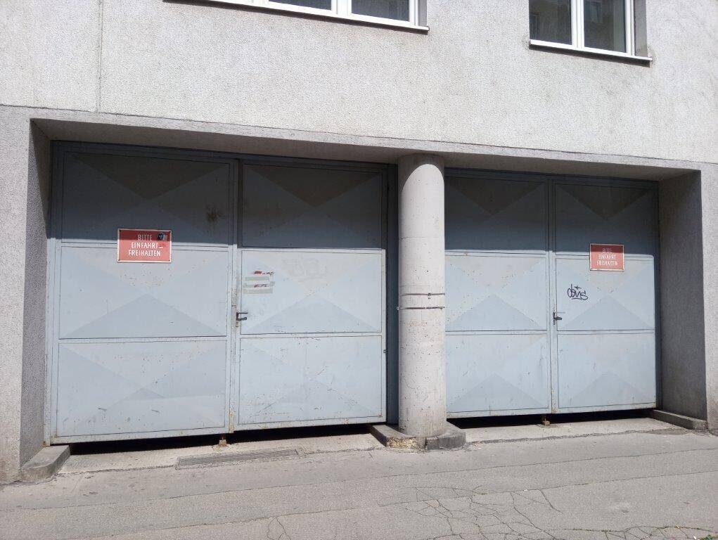 Zwei große graue Garagentore aus Metall, getrennt durch eine Betonsäule, mit Hinweisschildern.