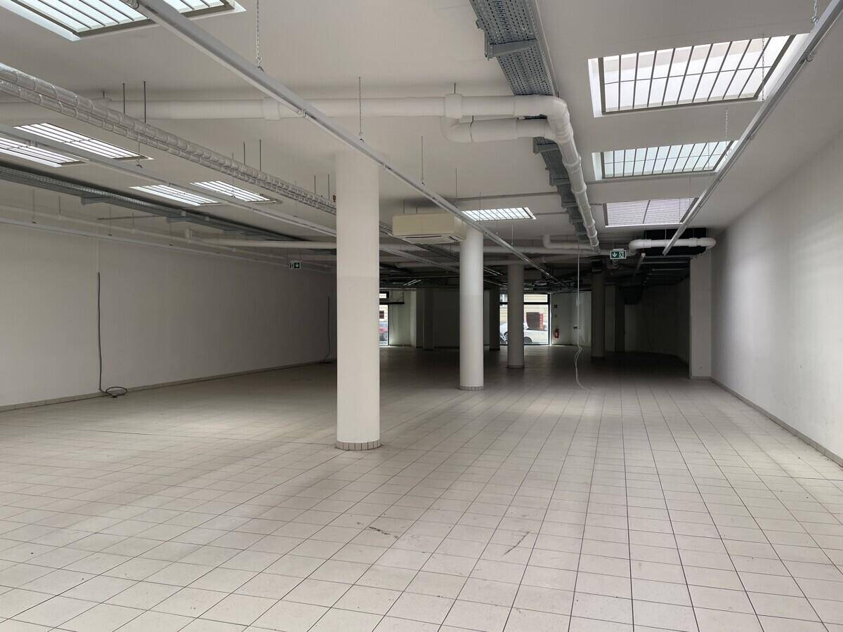 Großer, leerer Gewerberaum mit Fliesenboden, Säulen und sichtbaren Lüftungsrohren an der Decke.