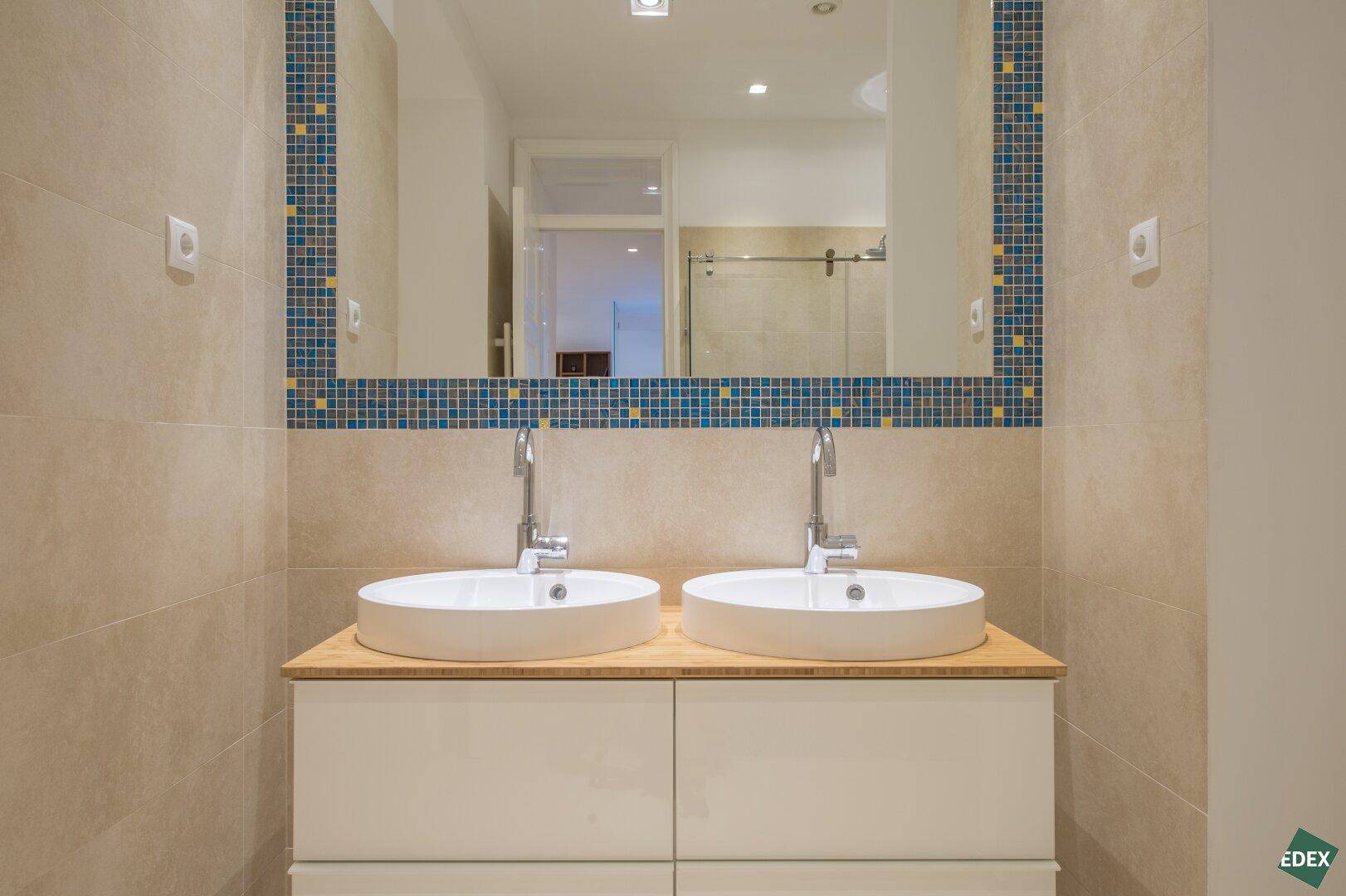 Doppelwaschbecken mit modernen Armaturen und einem großen Spiegel im Badezimmer.