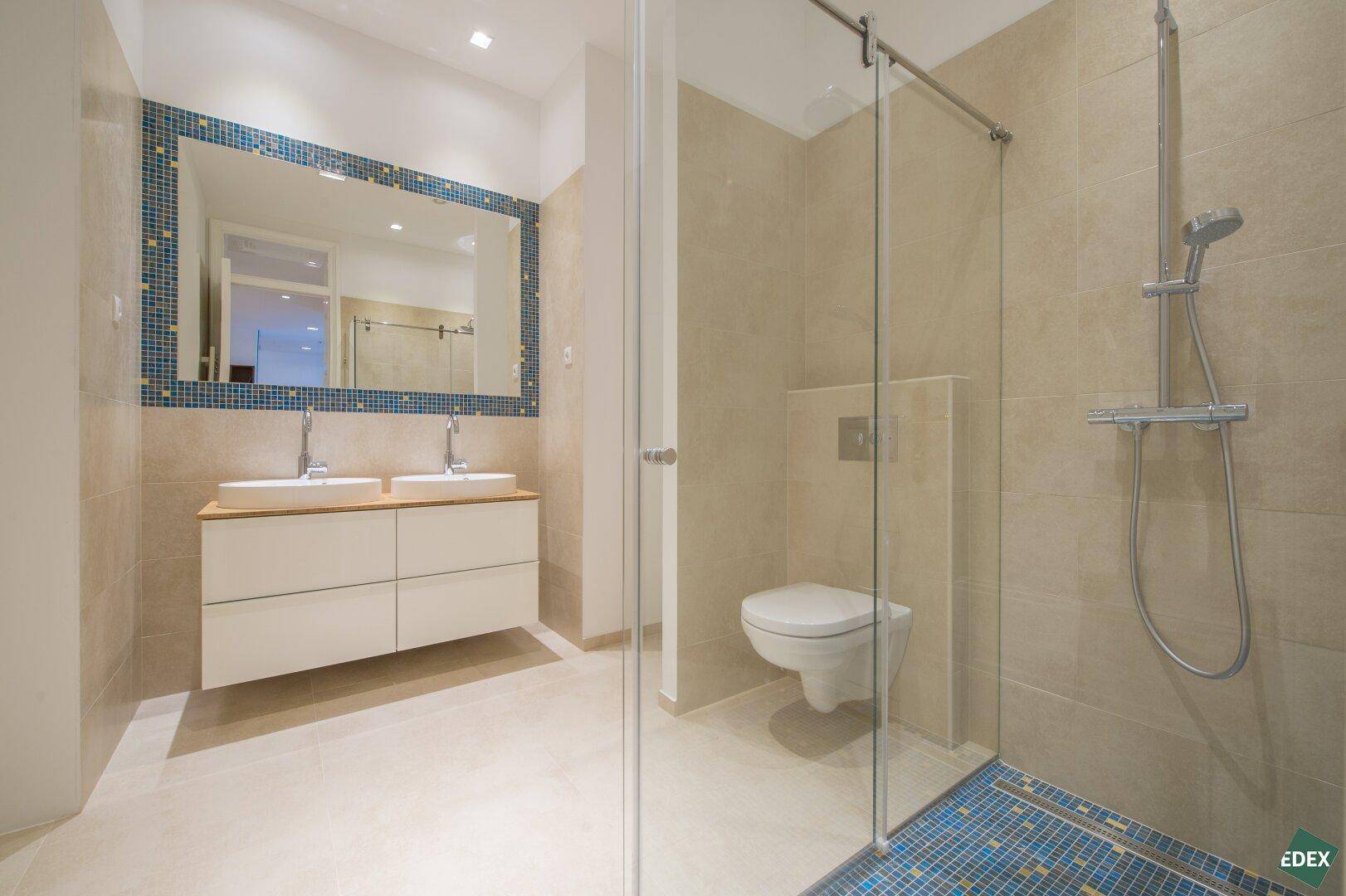 Modernes Badezimmer mit Doppelwaschbecken, begehbarer Dusche und blauen Mosaikfliesen.