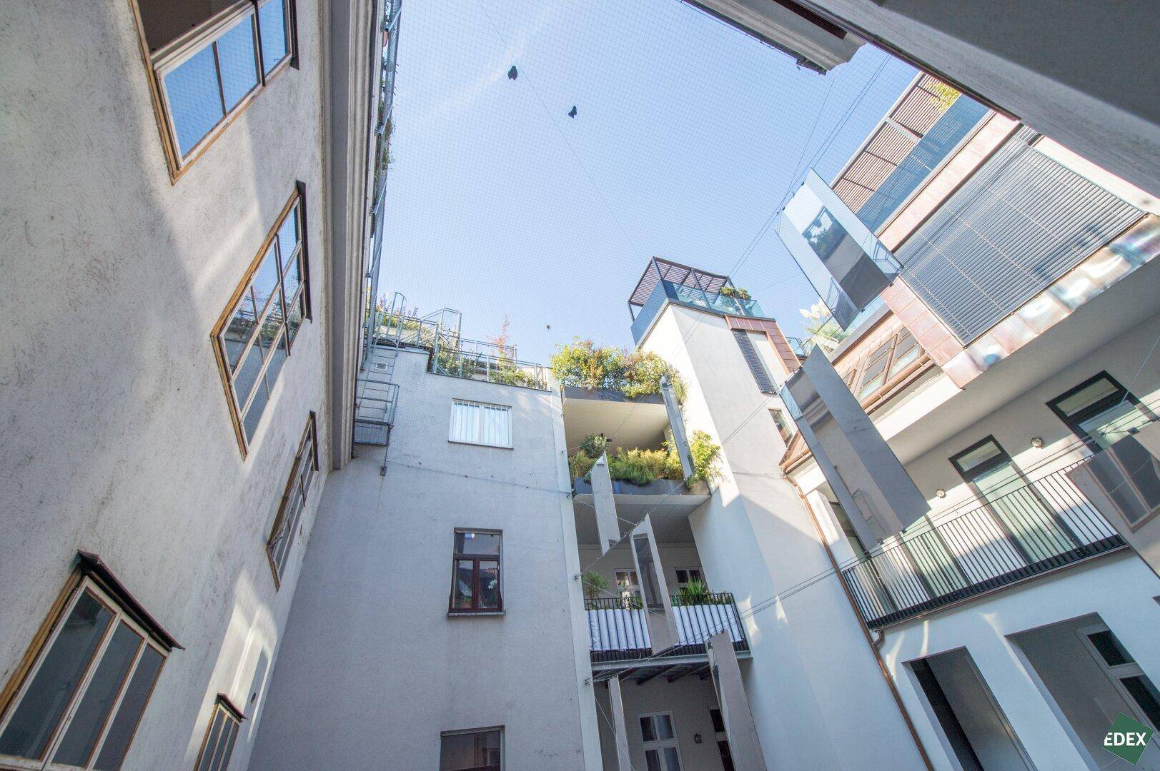 Blick nach oben in den hellen Innenhof mit modernen Gebäudefassaden und Dachterrassen.