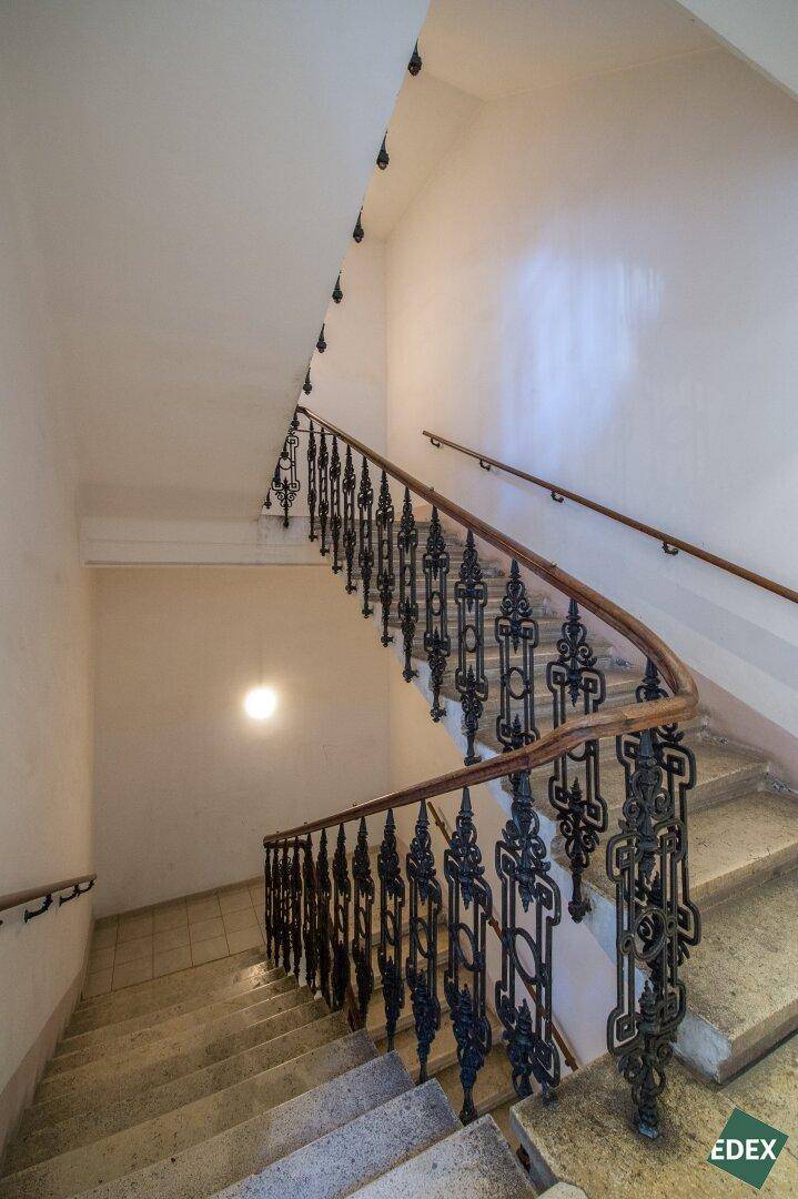 Historisches Treppenhaus mit schmiedeeisernem Geländer und Steinstufen.