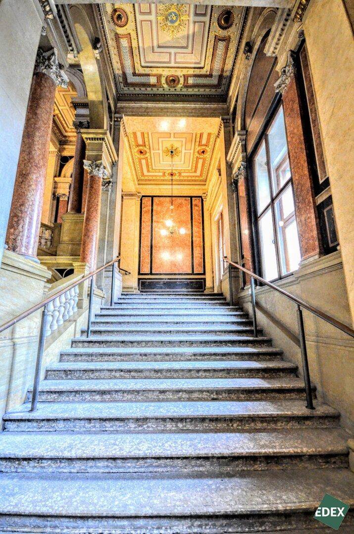 Prunkvolles Treppenhaus mit Marmorstufen und kunstvollen Verzierungen, das zu einer reich verzierten Decke führt.
