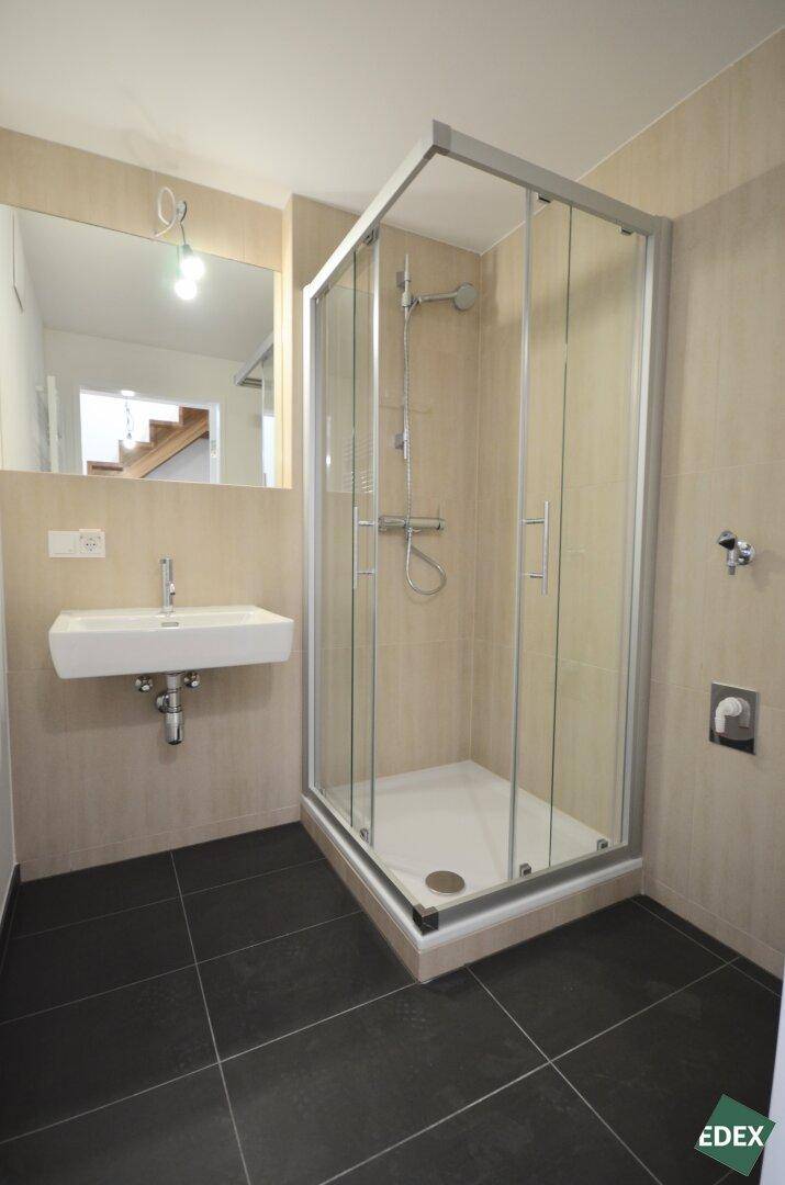 Modernes Badezimmer mit Duschkabine, wandhängendem Waschbecken und dunklen Bodenfliesen.