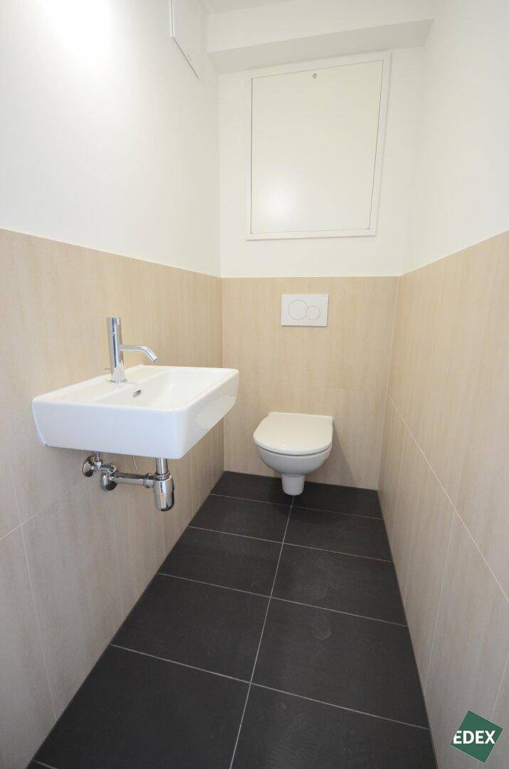 Kleines Gäste-WC mit wandhängendem WC, Waschbecken und dunklen Bodenfliesen.