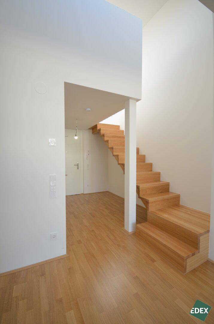Heller Flur mit einer modernen Holztreppe und durchgehendem Parkettboden.