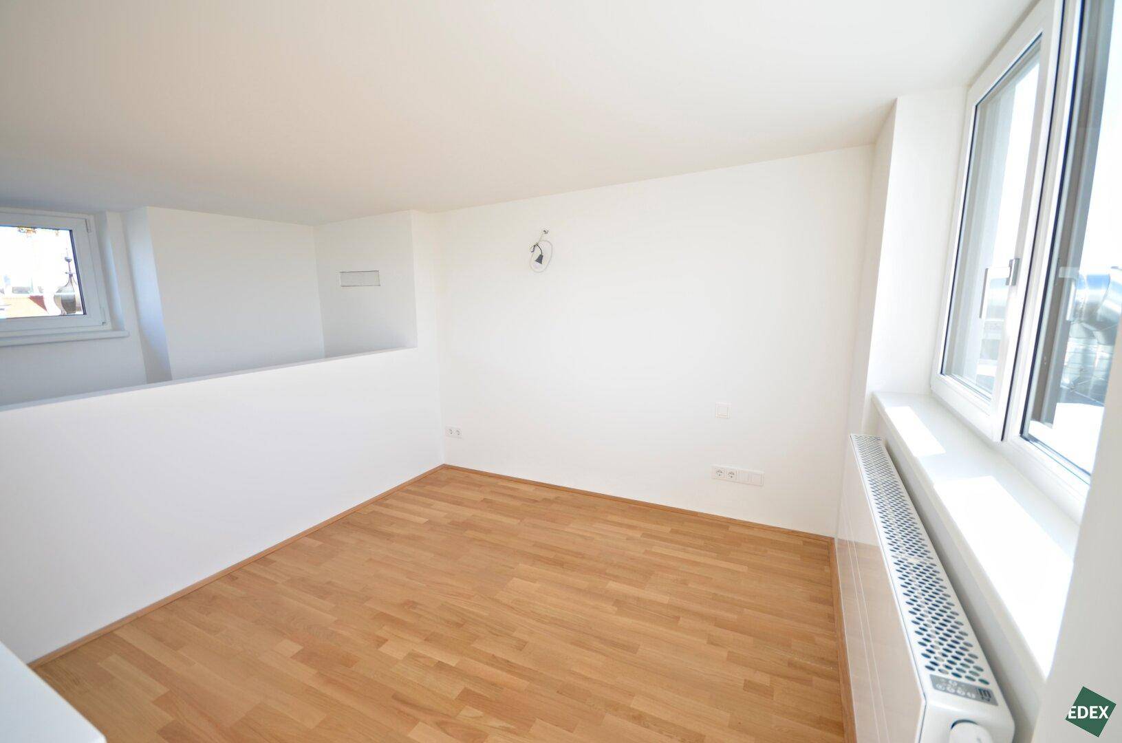 Heller Raum mit Holzboden und einem Fenster, das den Blick nach draußen freigibt.