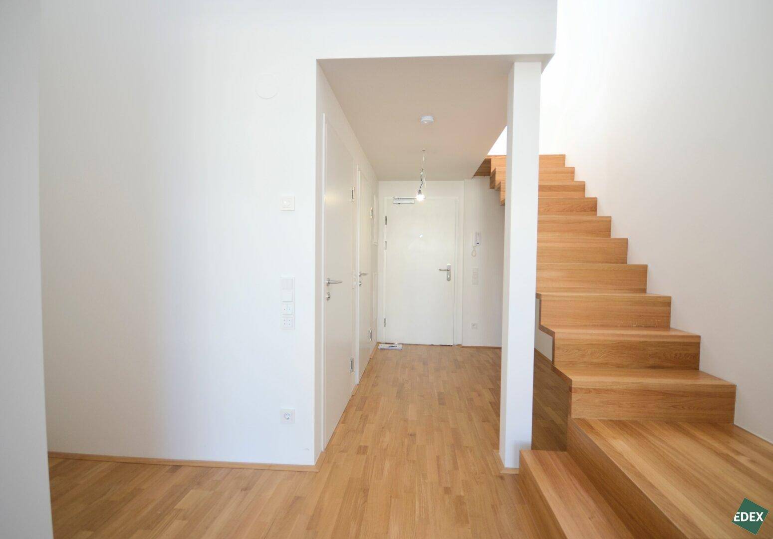 Geräumiger Flur mit Holzboden, weißen Türen und einer eleganten Holztreppe.