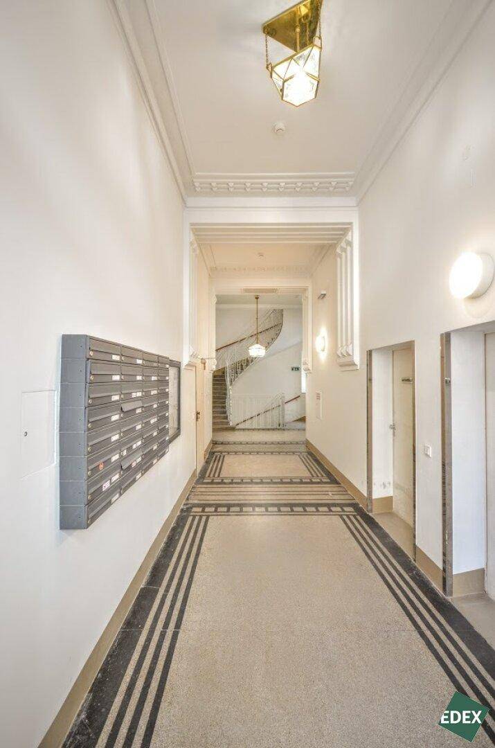 Langer Flur in einem Altbau mit dekorativem Boden, Briefkästen und Blick auf das Treppenhaus.