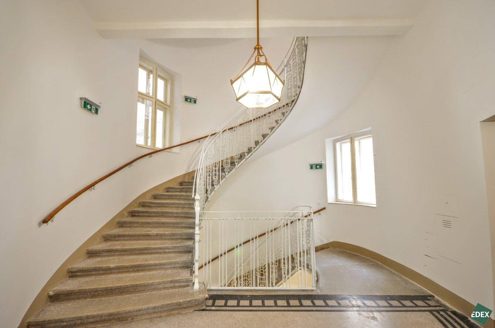Elegantes Treppenhaus in einem Altbau mit geschwungener Treppe und klassischer Beleuchtung.