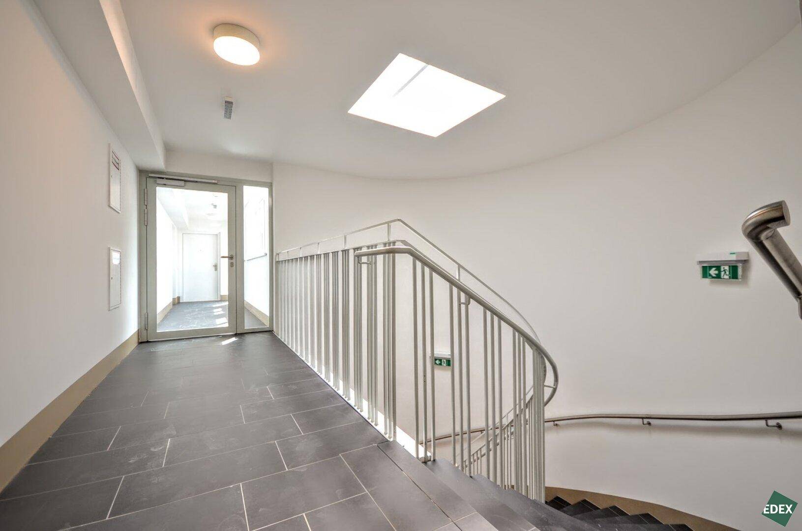 Modernes Treppenhaus mit Metallgeländer, dunklen Fliesen und einem Oberlicht für Tageslicht.