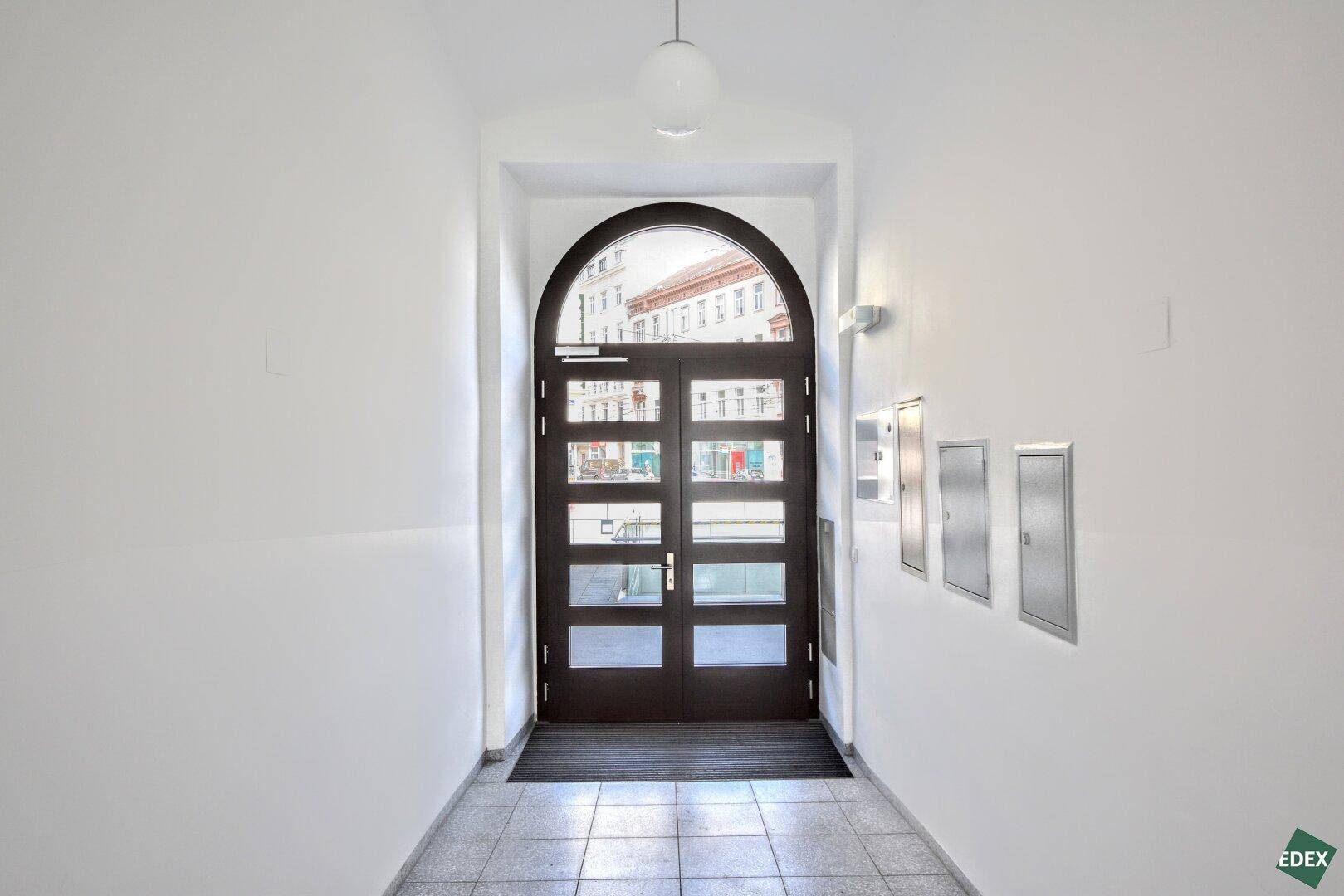 Repräsentativer Eingangsbereich mit großer Holztür und Bogenfenster, das den Blick zur Straße freigibt.