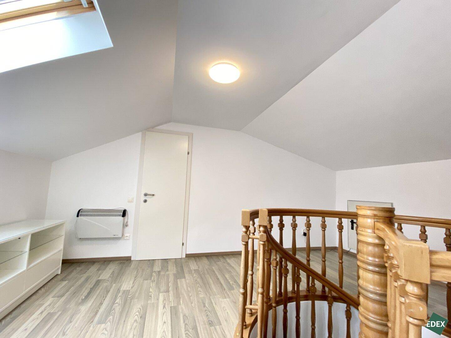 Heller Dachbodenbereich mit Laminatboden, Dachfenster und Zugang zu weiteren Räumen.