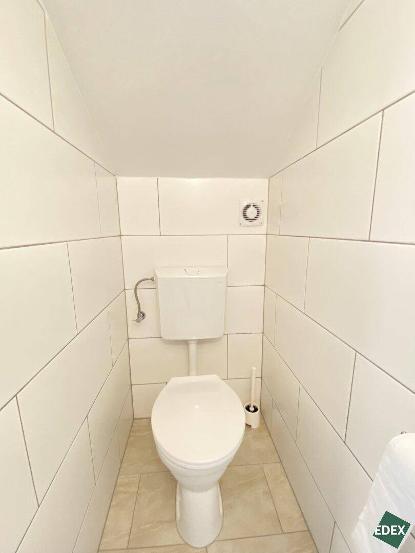 Kleine Gästetoilette mit weißen Fliesen und Lüftungsventil an der Wand.