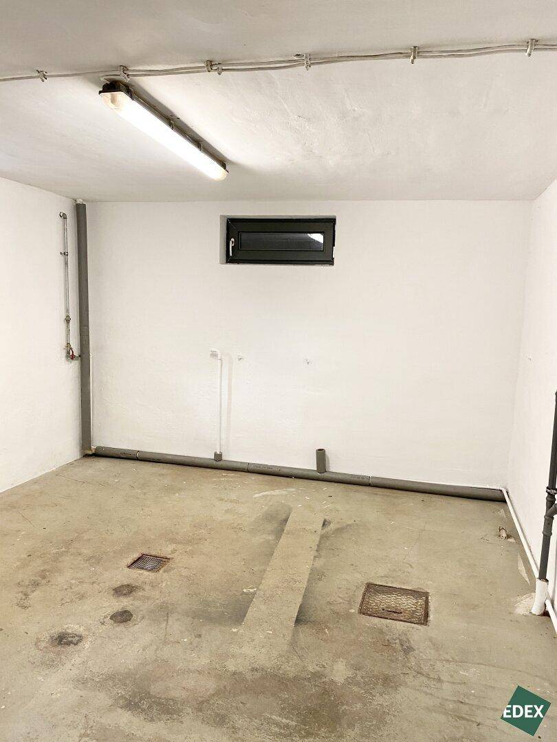 Leerer Kellerraum mit Betonboden, kleinem Fenster und sichtbaren Installationen an den Wänden.