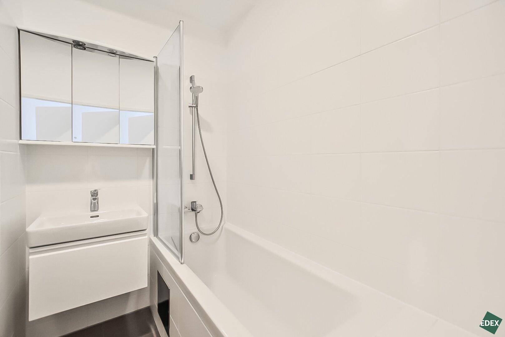 Modernes Badezimmer mit Badewanne, Duschabtrennung aus Glas und weiß gefliesten Wänden.