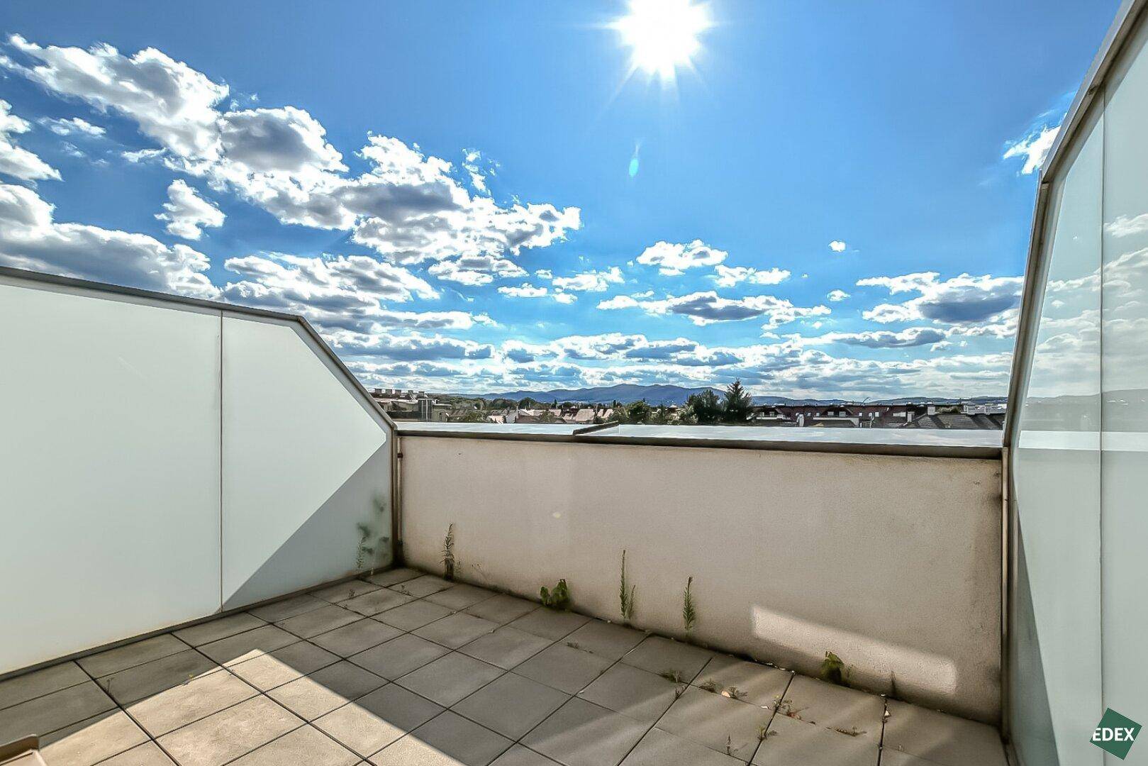 Sonniger Außenbereich mit Fliesenboden und Blick auf die umliegende Landschaft und Berge.