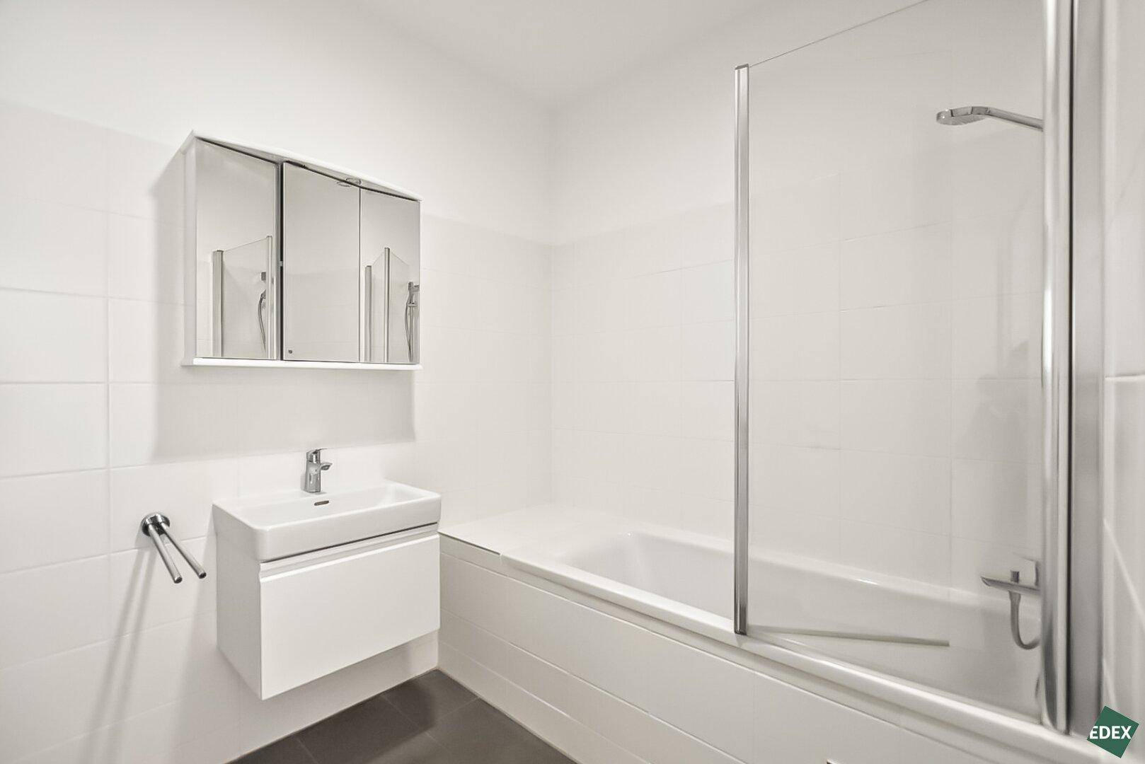 Helles Badezimmer mit Badewanne, Waschbeckenunterschrank und Spiegelschrank über dem Waschtisch.