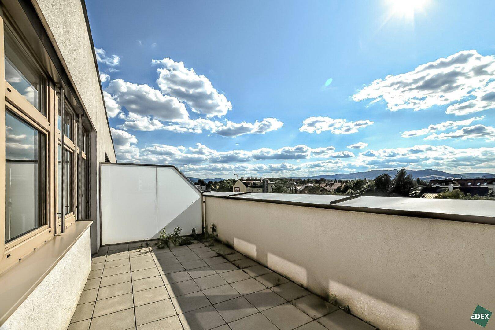 Geräumige Terrasse mit Fliesenboden und weitem Blick über die Landschaft und Berge unter blauem Himmel.