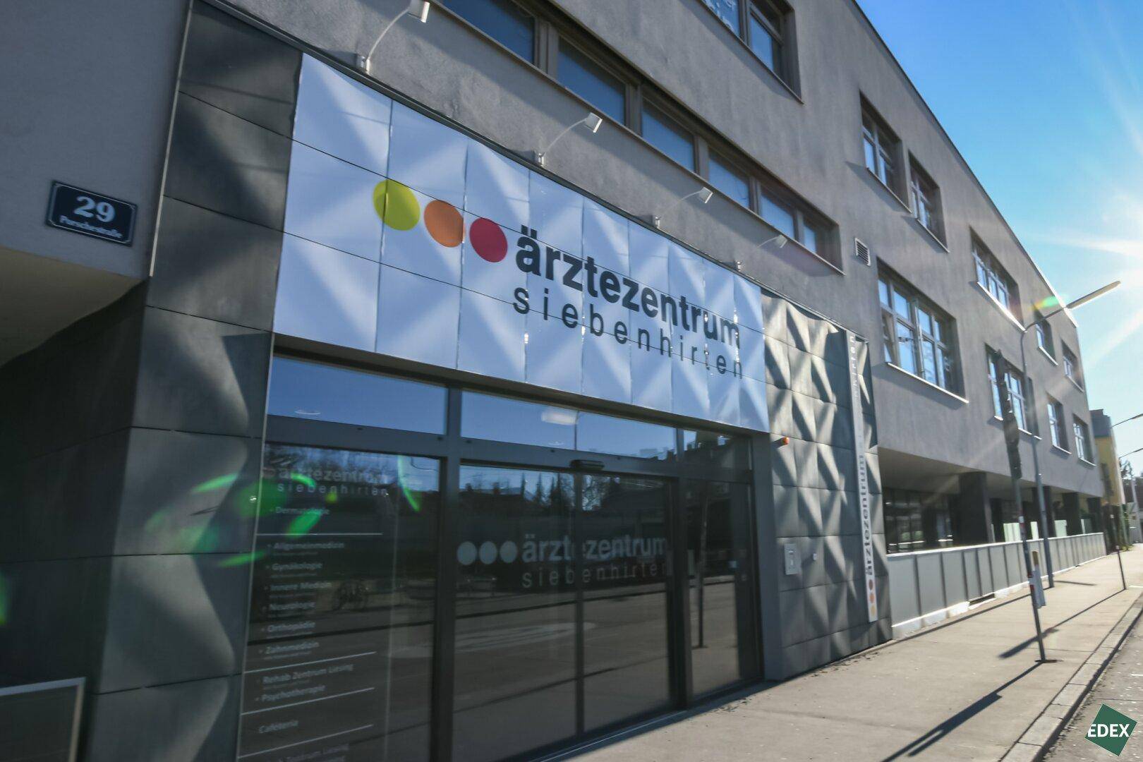 Eingangsbereich eines modernen Ärztezentrums mit großer Beschilderung, strukturierter Fassade und viel Glas.